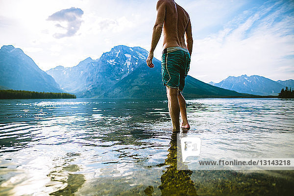 Low section of man standing in lake against mountains and sky