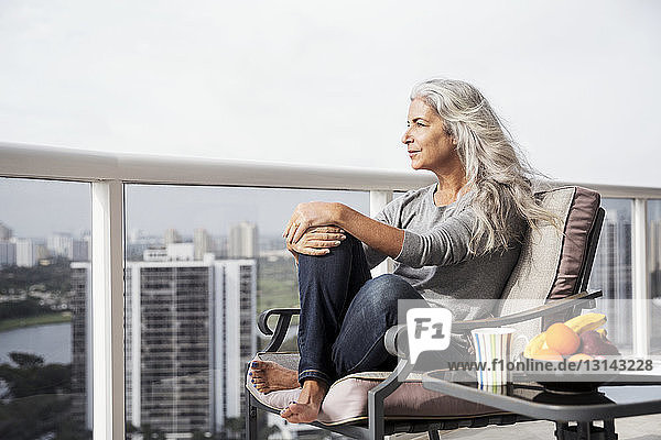 Nachdenkliche reife Frau sitzt auf einem Stuhl auf dem Balkon
