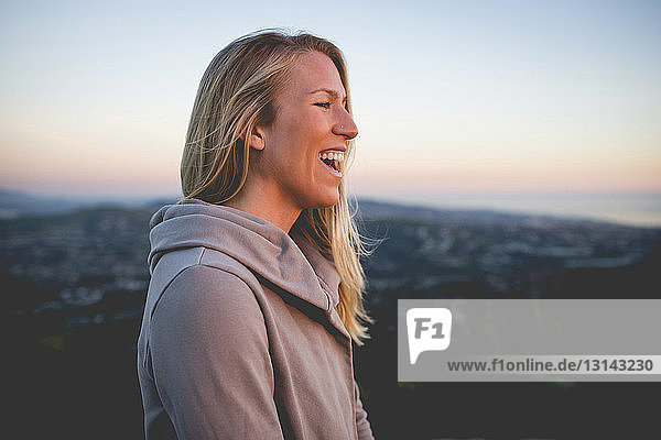 Side view of happy woman standing on mountain against sky during sunset