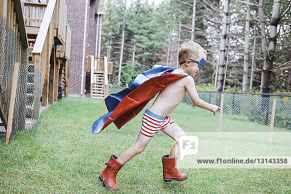 Side view of shirtless boy wearing cape and eye patch while playing in yard