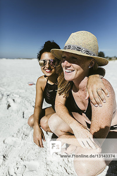 Cheerful female friends crouching at beach during sunny day