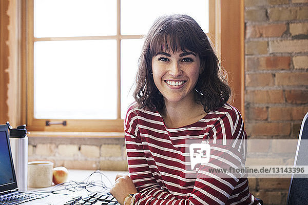 Porträt einer lächelnden Geschäftsfrau  die im Büro am Schreibtisch sitzt