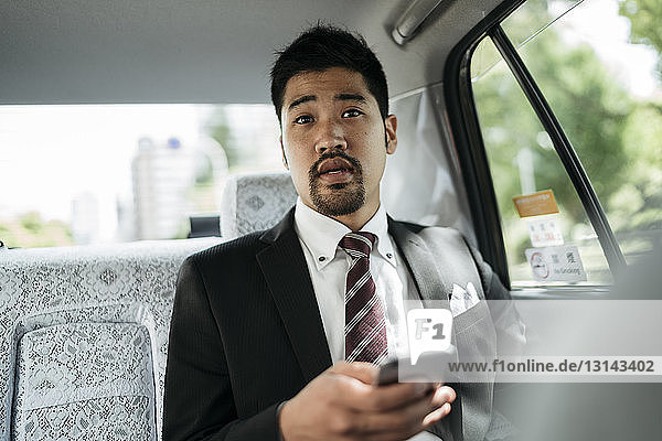 Junger Geschäftsmann hält Smartphone in der Hand  während er im Taxi sitzt