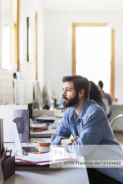Thoughtful businessman sitting at desk in creative office