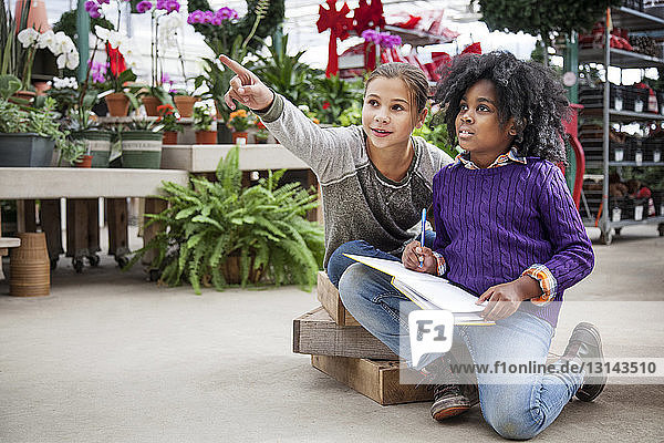 Girl pointing while sitting with friend in plant nursery