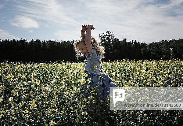 Happy girl with arms raised standing amidst plants against sky