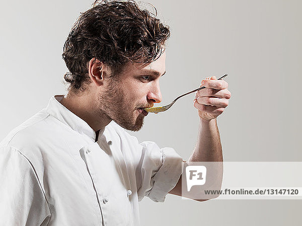 Chef tasting food from spoon against white background