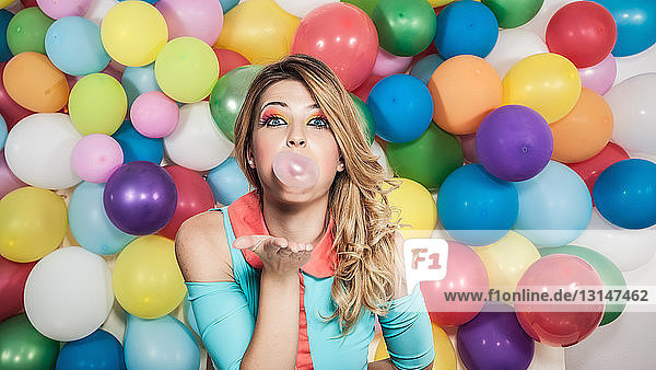 Junge Frau steht vor bunten Luftballons und bläst Blasen mit Kaugummi