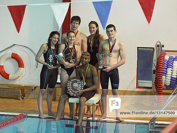 Swimmers holding trophies at pool