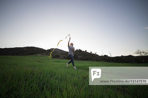 Junge Frau läuft auf einem Feld und hält ein Tanzband hoch