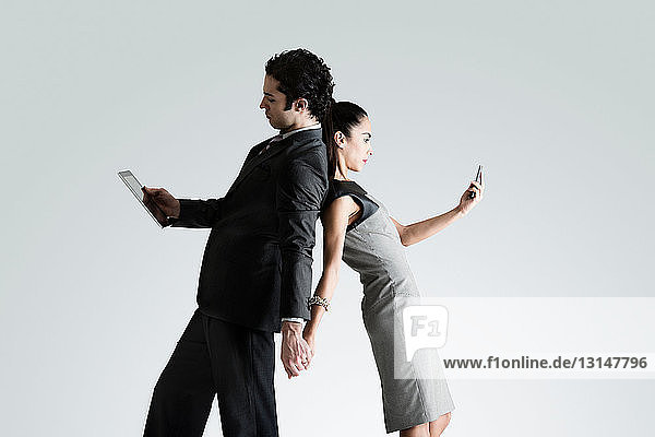 Business couple using cell phone and digital tablet  back to back