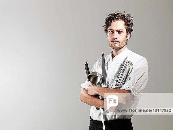 Chef holding kitchen utensils against white background