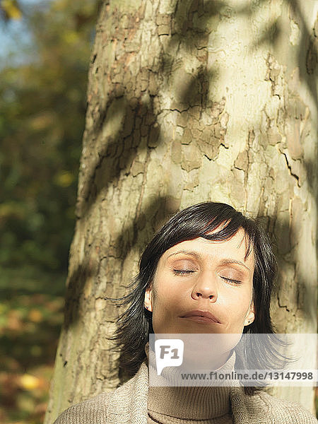 Frau lehnt im Sonnenschein an einem Baum