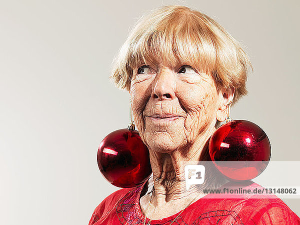 Senior woman wearing red baubles as earrings against white background