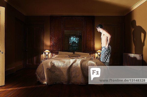 Mann in Pyjamahose am Bett stehend