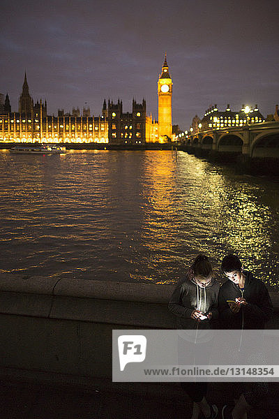 Blick von oben auf junge Frauen  die von einem Smartphone beleuchtet werden  gegenüber dem Palace of Westminster  London  UK