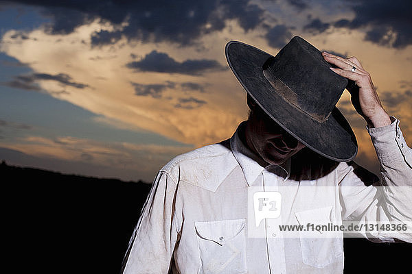 Porträt eines Cowboys  der bei Sonnenuntergang sein Gesicht mit einem Stetson beschattet  Nevada  USA