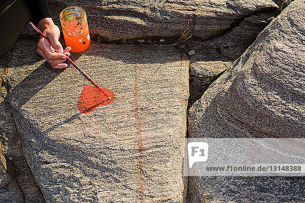 Person malt Herz auf Felsen
