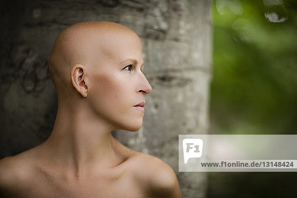 Aktporträt einer jungen Frau mit Krebs  die sich an einen Baumstamm lehnt