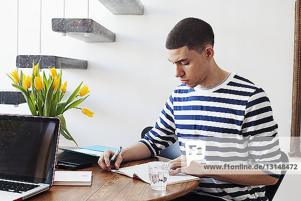 Young man sitting at table  writing in notebook