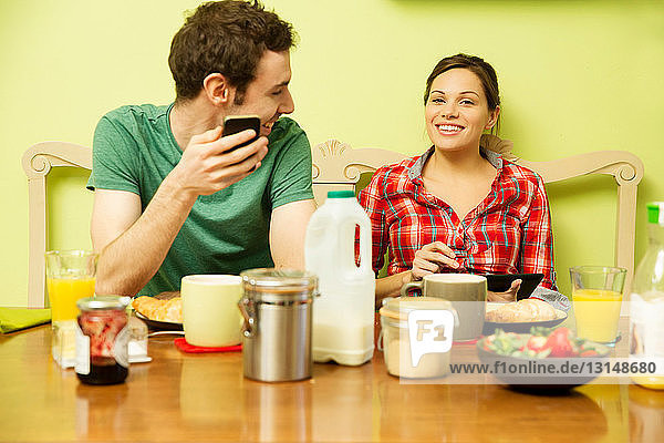 Junges Paar beim Frühstück  Mann mit Smartphone