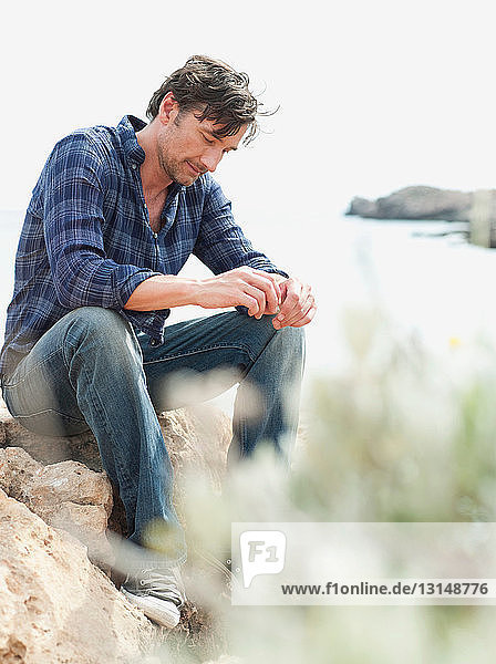 Mann sitzt auf Felsen an Klippen