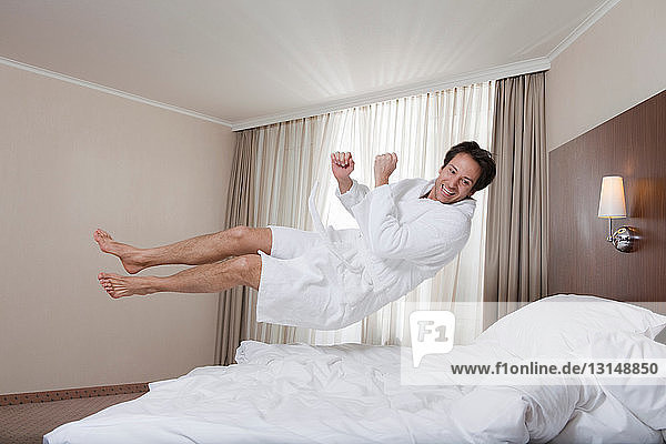businessman in bathrobe jumping on bed