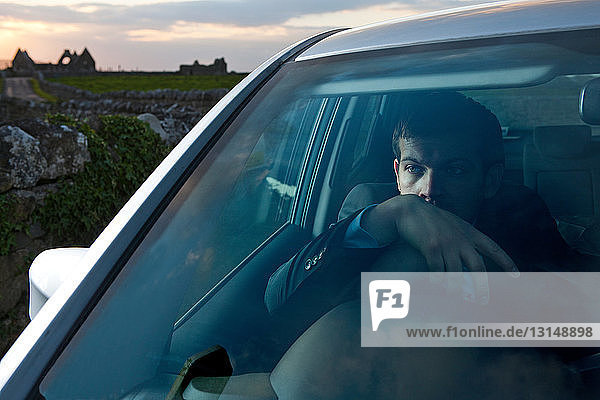 Businessman leaning on steering wheel in car