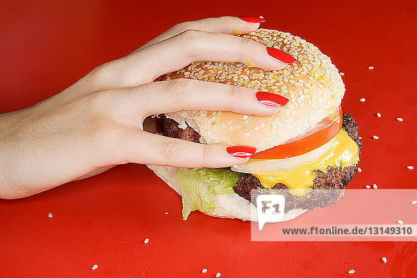 Frau mit roten Fingernägeln hält Burger