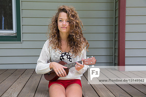 Teenage girl sitting on porch holding miniature guitar