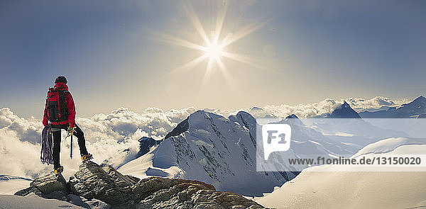 Panoramic view of male climber looking out from snow covered mountain top  Swiss Alps  Switzerland