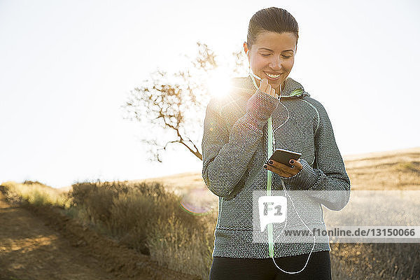 Ältere Läuferin auf einem sonnenbeschienenen Hügel  die die Musik ihres Smartphones auswählt