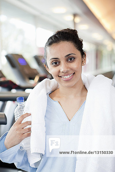 Frau mit Handtuch und Wasserflasche im Fitnessstudio