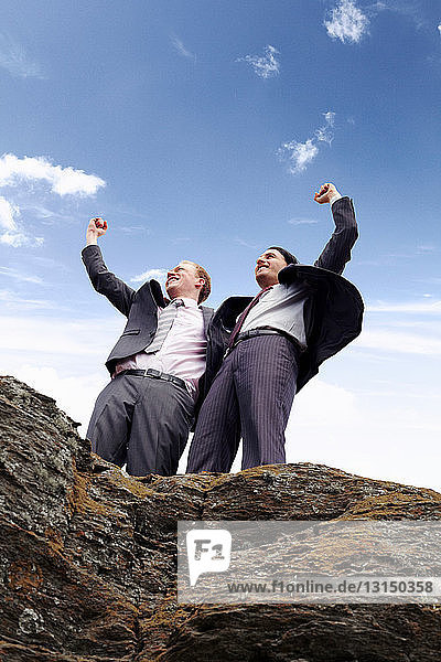 Businessmen cheering on cliff edge