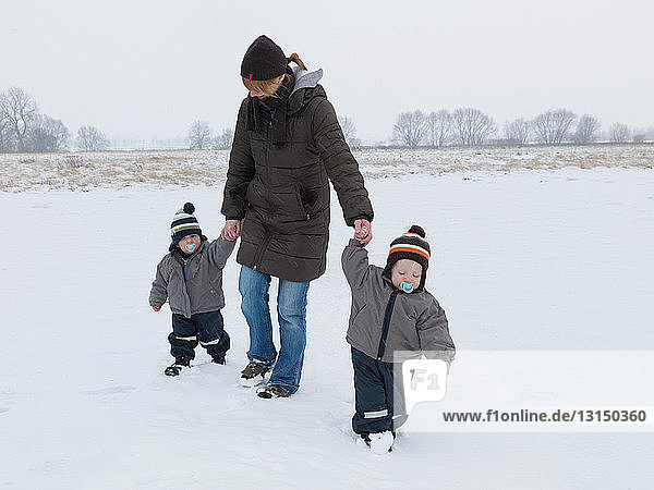 Frau geht mit Zwillingssöhnen im Schnee spazieren