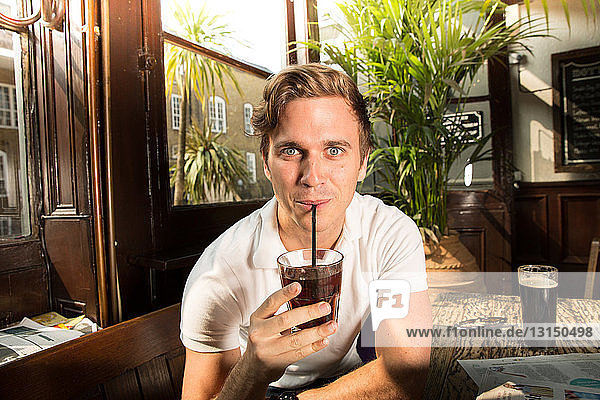 Portrait of young man drinking through straw  looking at camera