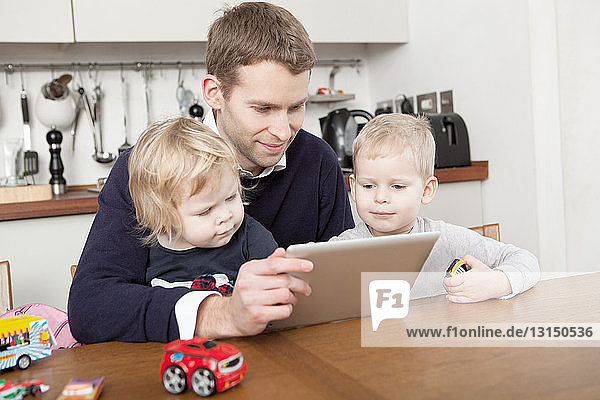 Father using digital tablet with son and daughter
