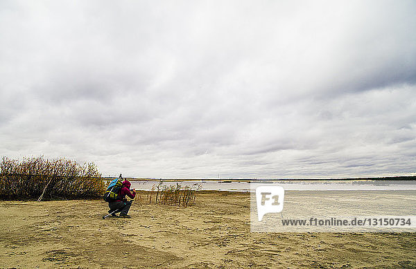 Junger Mann beim Wandern  hockend  fotografiert Seeblick  Rückansicht