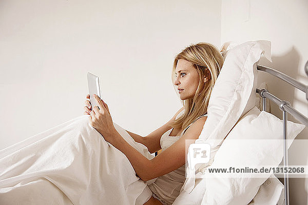 Mittlere erwachsene Frau  die im Bett sitzt und ein digitales Tablet benutzt