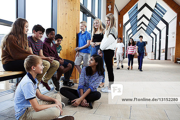 Group of teenage schoolchildren sitting chatting in corridor