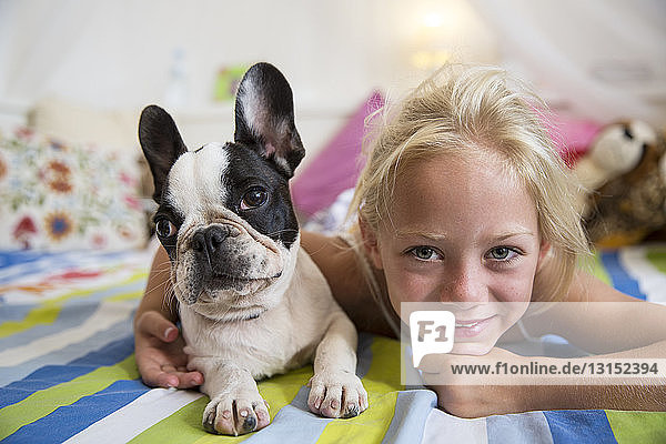 Porträt eines Mädchens und eines niedlichen Hundes auf dem Bett liegend