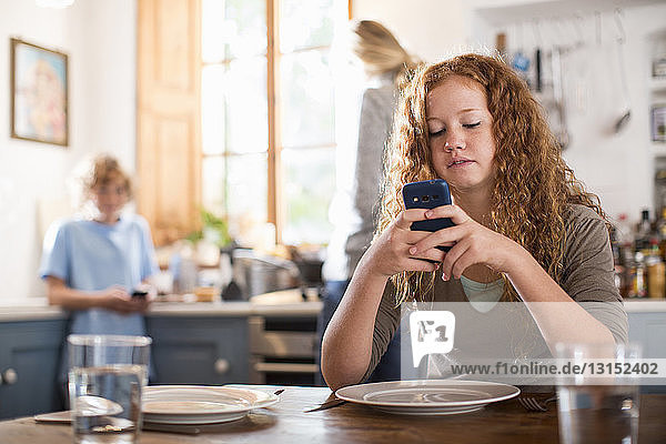 Teenager-Mädchen benutzt Smartphone am Esstisch