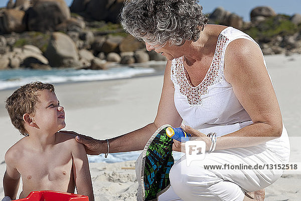 Frau sitzt mit Enkel am Strand