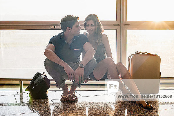 Junges Paar sitzt auf einem Geländer im Flughafen
