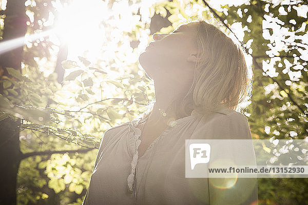 Mature woman standing in stream of light in forest