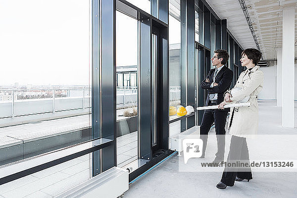 Architects looking out of window with blueprint