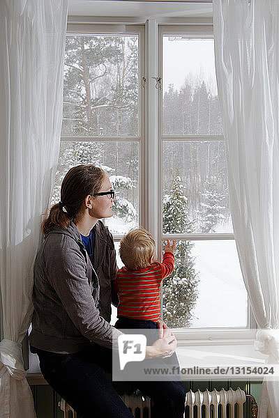 Mutter und Baby im Fenster mit Blick auf den Schnee