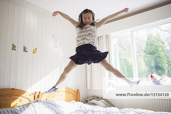 Junges Mädchen springt mitten in der Luft auf dem Bett