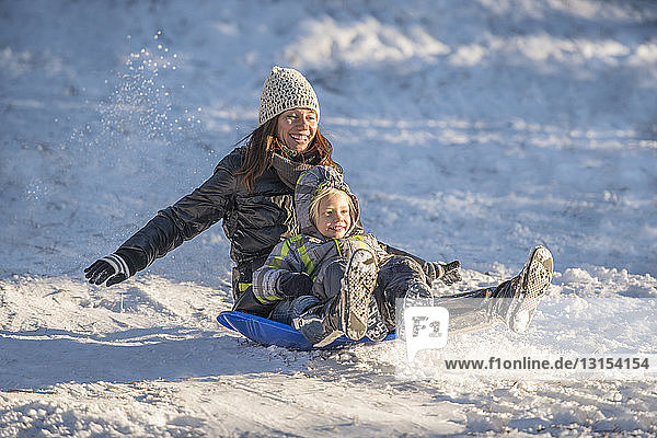 Porträt einer lächelnden Mutter und ihres Sohnes beim Schlittenfahren im Schnee