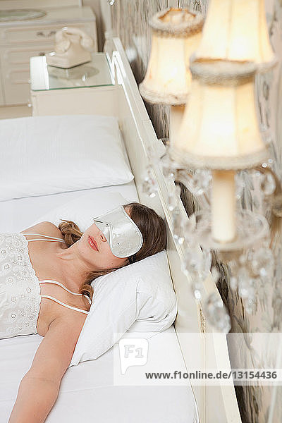 Frau auf Hotelbett mit Schlafmaske